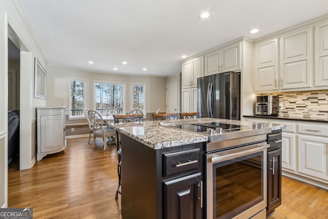 kitchen featuring recessed lighting, a breakfast bar, light wood-style floors, appliances with stainless steel finishes, and decorative backsplash