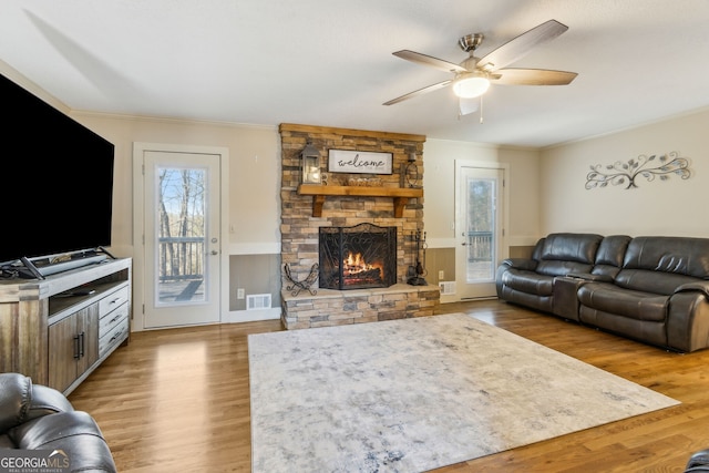 living room featuring a stone fireplace, ornamental molding, wood finished floors, and visible vents