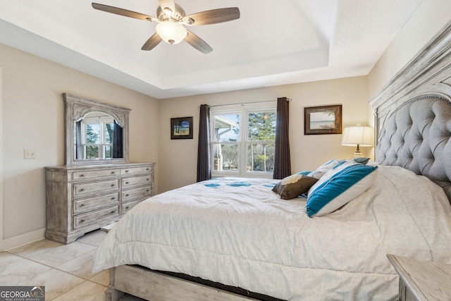 bedroom featuring light tile patterned floors, baseboards, a raised ceiling, and a ceiling fan