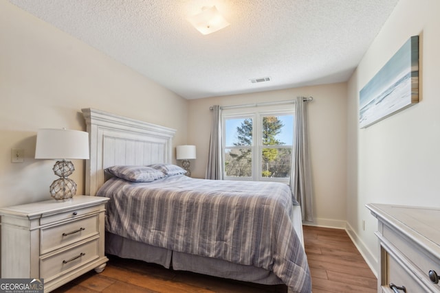 bedroom featuring dark wood-style floors, visible vents, a textured ceiling, and baseboards