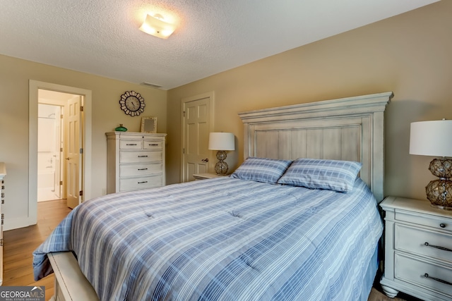 bedroom with a textured ceiling, visible vents, and wood finished floors