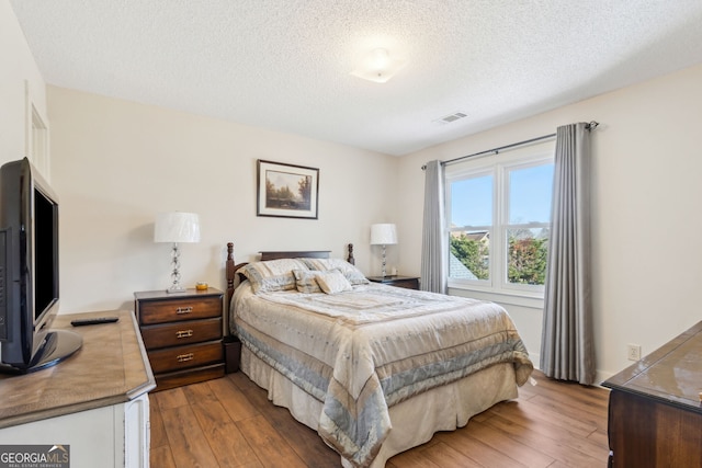 bedroom with hardwood / wood-style flooring, visible vents, and a textured ceiling