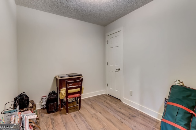 misc room with a textured ceiling, light wood finished floors, and baseboards