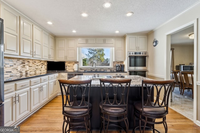 kitchen featuring a center island, decorative backsplash, appliances with stainless steel finishes, light wood-style floors, and a kitchen breakfast bar