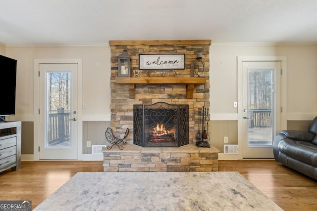 living area with visible vents, wood finished floors, a stone fireplace, and ornamental molding