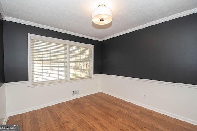 empty room with crown molding, visible vents, a textured ceiling, baseboards, and hardwood / wood-style flooring