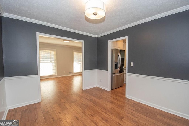 empty room featuring a textured ceiling, ornamental molding, a wainscoted wall, and wood-type flooring