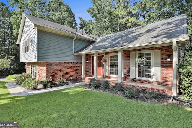 split level home featuring covered porch, roof with shingles, a front lawn, and brick siding