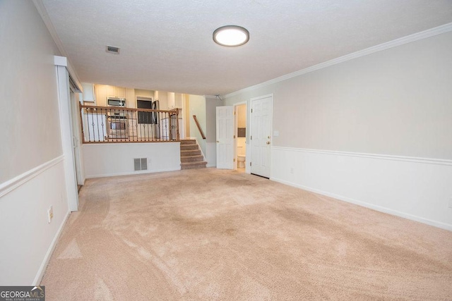 unfurnished living room featuring carpet floors, visible vents, ornamental molding, and stairs