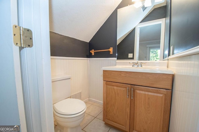 bathroom with lofted ceiling, toilet, wainscoting, vanity, and tile patterned flooring