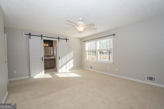 interior space with ceiling fan, a barn door, light colored carpet, visible vents, and baseboards