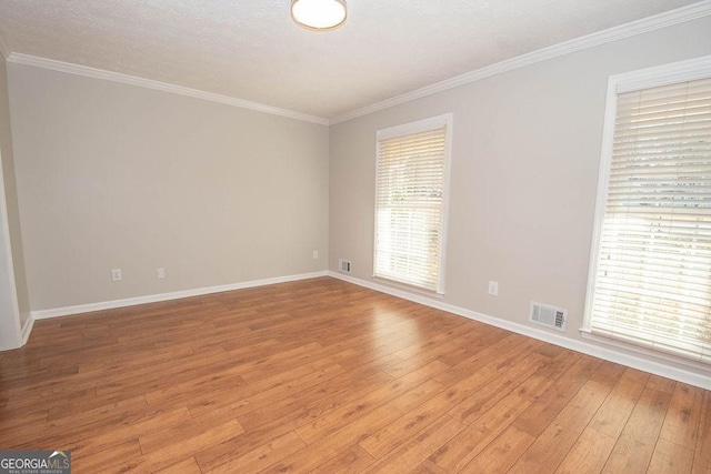 empty room with light wood-type flooring, visible vents, and ornamental molding