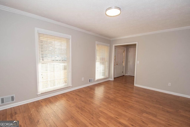 unfurnished room with baseboards, crown molding, visible vents, and hardwood / wood-style floors