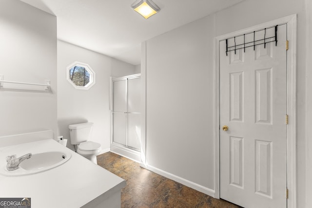 bathroom with a stall shower, baseboards, toilet, stone finish flooring, and vanity