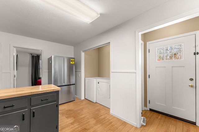 kitchen featuring light wood-style flooring, a wainscoted wall, butcher block counters, freestanding refrigerator, and washer and clothes dryer