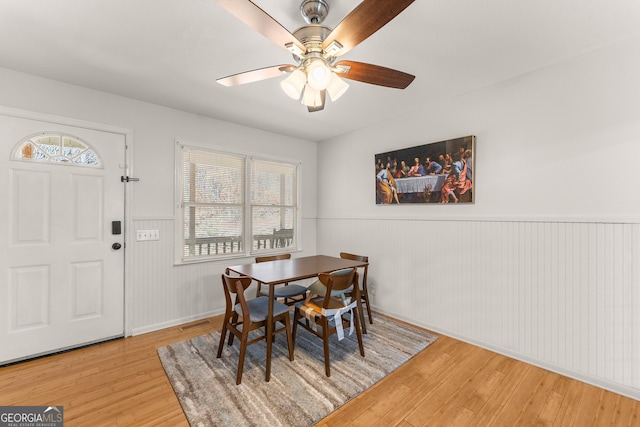 dining area with a wainscoted wall, ceiling fan, visible vents, and wood finished floors