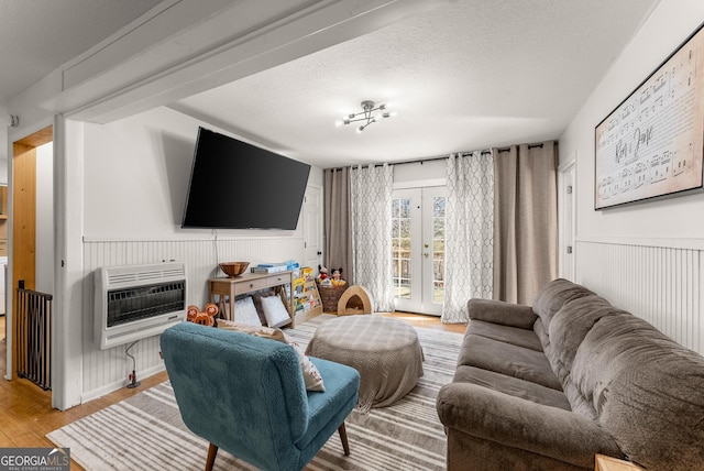 living area featuring french doors, a wainscoted wall, heating unit, light wood-style flooring, and a textured ceiling