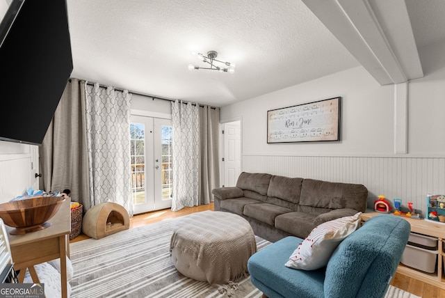 living room with a textured ceiling, french doors, wainscoting, and wood finished floors