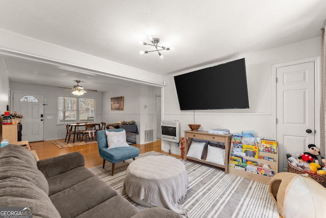 living room with ceiling fan with notable chandelier, wood finished floors, visible vents, and heating unit