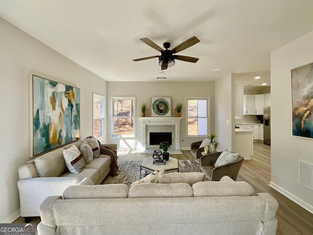 living room with a premium fireplace, light wood-type flooring, visible vents, and baseboards