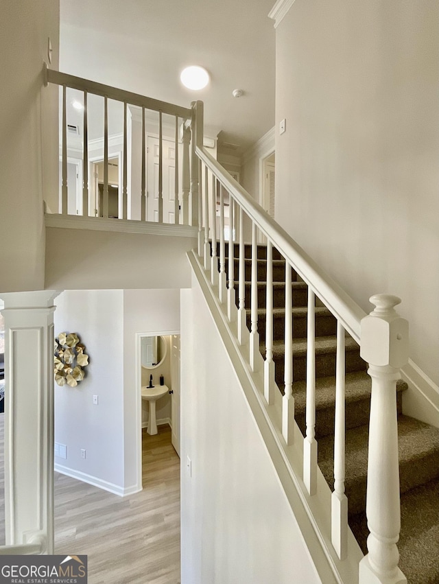 stairway featuring crown molding, decorative columns, baseboards, and wood finished floors