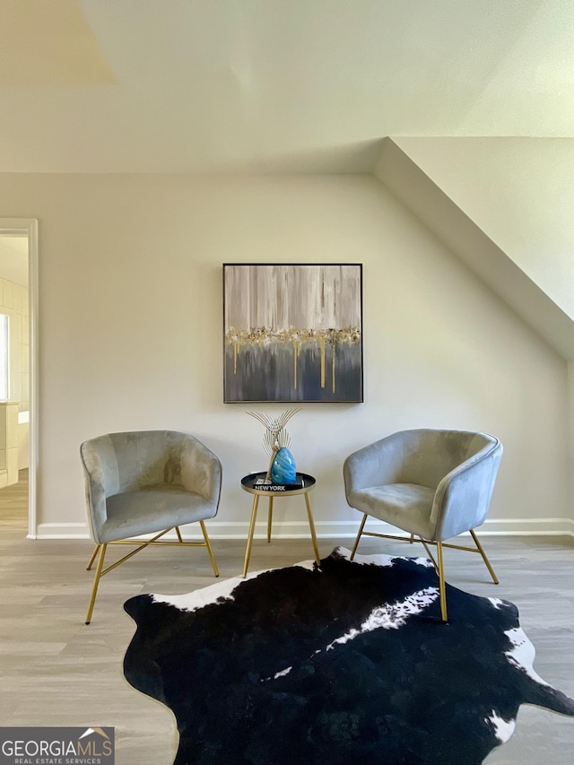 sitting room featuring lofted ceiling, baseboards, and wood finished floors