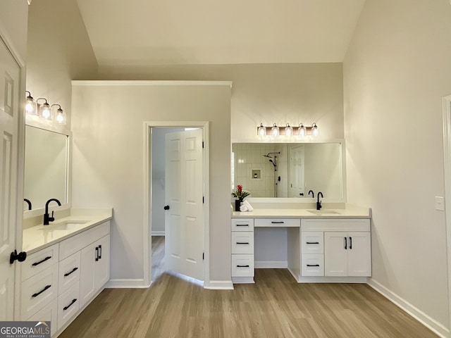 full bath featuring two vanities, a sink, tiled shower, and wood finished floors