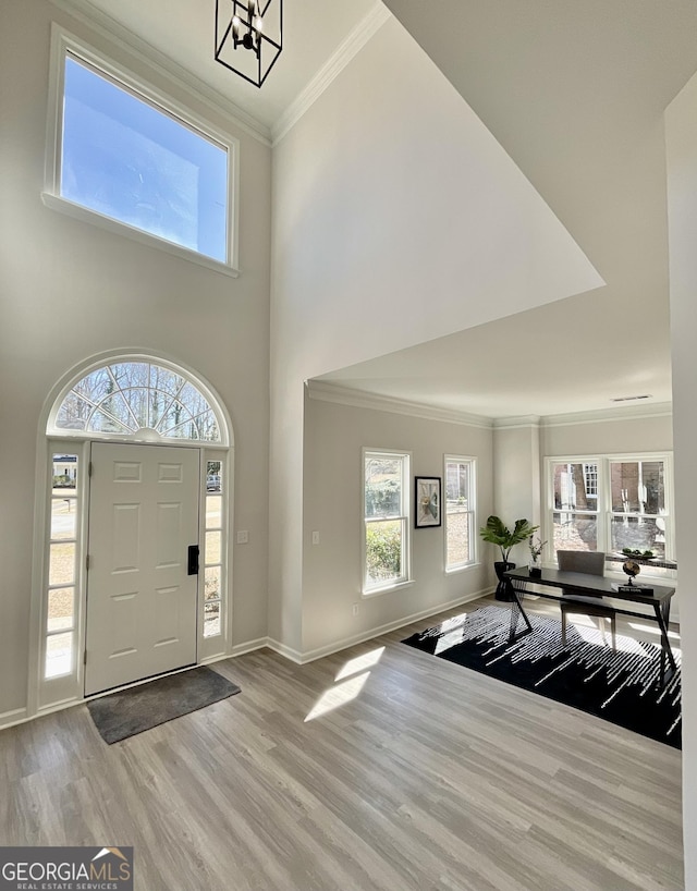 foyer with a notable chandelier, a towering ceiling, baseboards, light wood finished floors, and crown molding