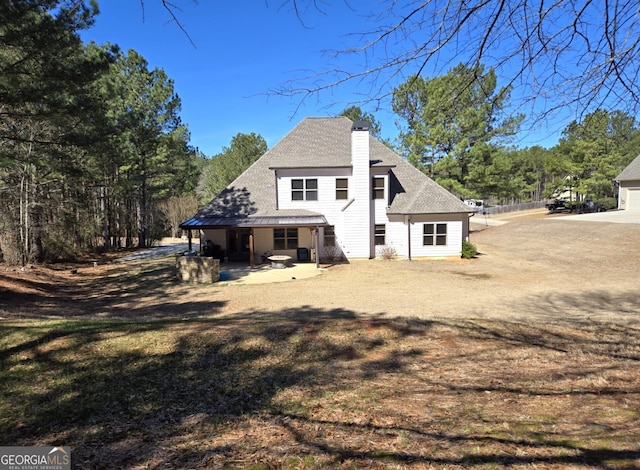 back of house featuring roof with shingles, a chimney, and a patio area