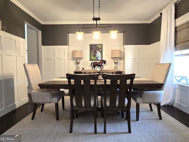 dining space featuring a wainscoted wall, crown molding, a decorative wall, and wood finished floors