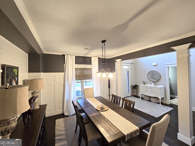 dining area featuring ornate columns, dark wood finished floors, crown molding, and wainscoting