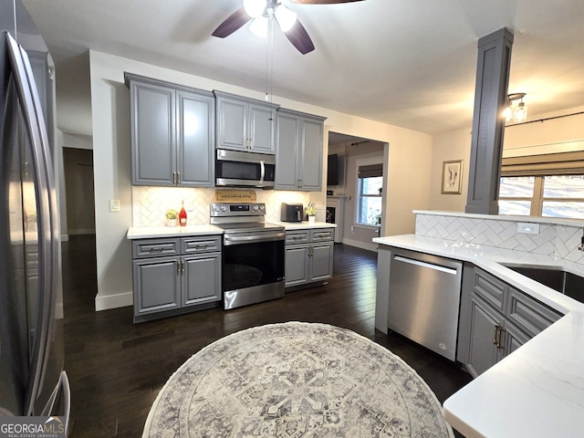 kitchen with gray cabinetry, a sink, light countertops, appliances with stainless steel finishes, and decorative columns