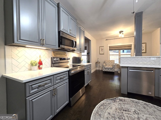 kitchen with appliances with stainless steel finishes, dark wood-style flooring, light countertops, gray cabinetry, and backsplash