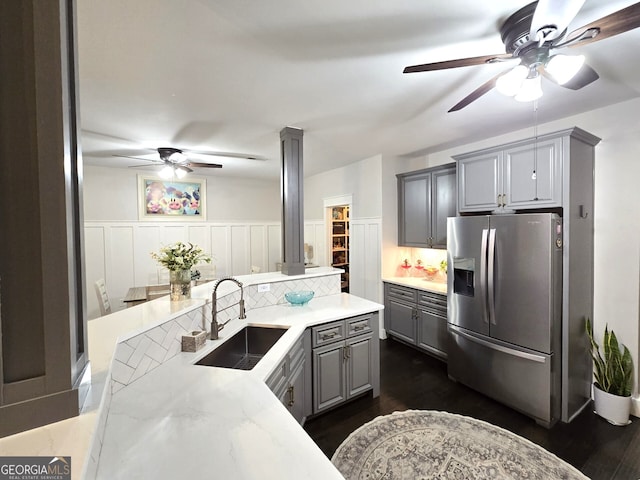 kitchen with ceiling fan, gray cabinetry, a wainscoted wall, a sink, and stainless steel fridge