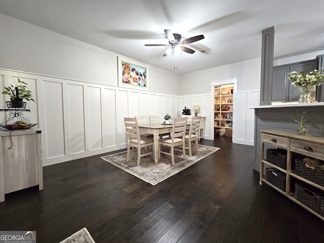 dining space featuring wainscoting, ceiling fan, dark wood finished floors, and a decorative wall