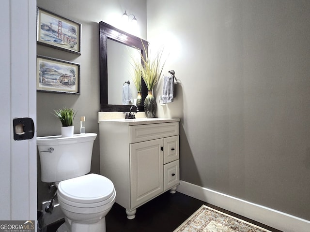 half bath with baseboards, vanity, and toilet