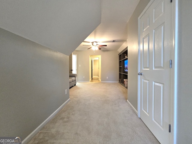 corridor featuring light carpet, built in shelves, and baseboards