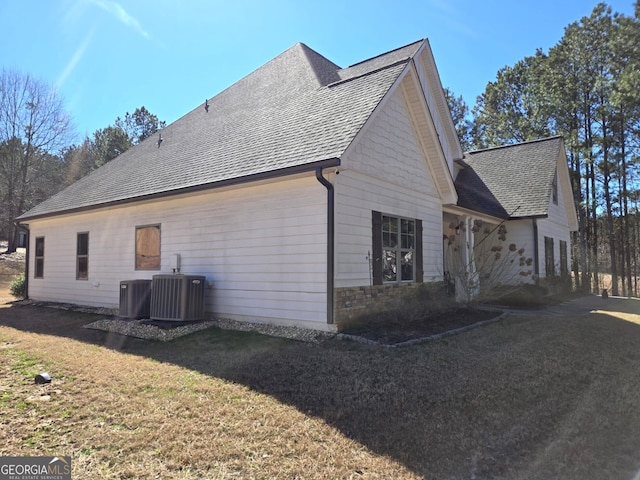 view of property exterior featuring central AC unit, a lawn, and roof with shingles