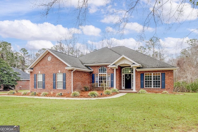 view of front facade featuring a shingled roof, a front yard, and brick siding