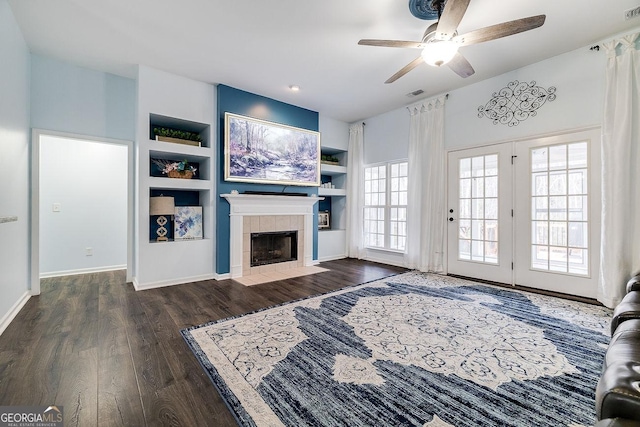 living area with built in features, dark wood finished floors, visible vents, a tiled fireplace, and baseboards