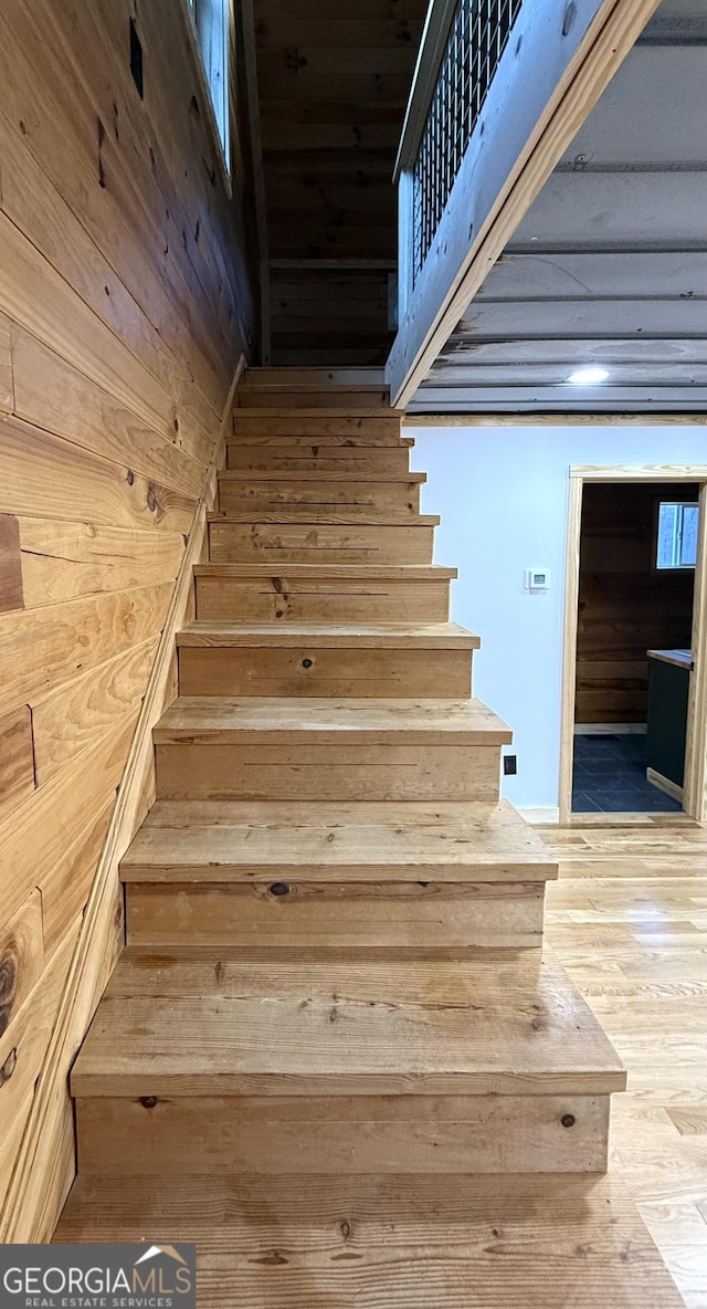 stairway with wooden walls and wood finished floors