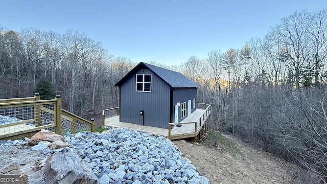 view of side of home featuring a deck, a forest view, and roof with shingles