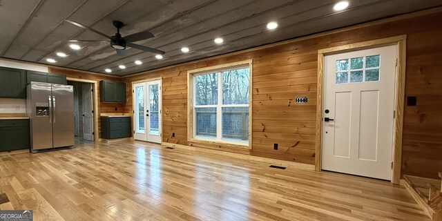 kitchen with light wood-style floors, light countertops, wood walls, and stainless steel fridge with ice dispenser