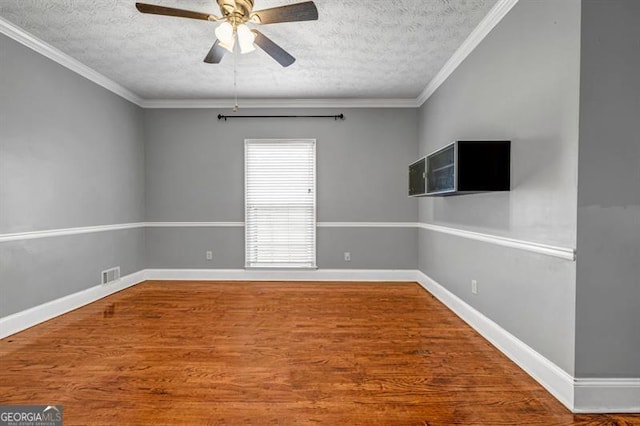 unfurnished room featuring a textured ceiling, wood finished floors, visible vents, baseboards, and ornamental molding