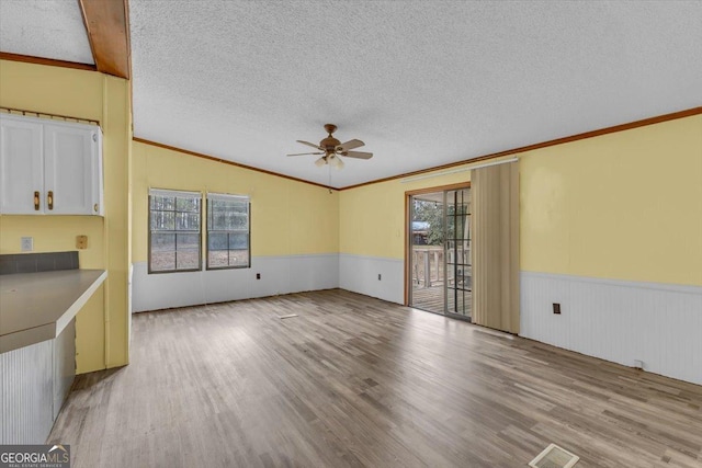 unfurnished living room with light wood-type flooring, a wainscoted wall, ornamental molding, and a textured ceiling