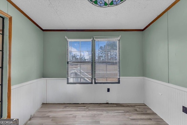 empty room featuring a wainscoted wall, a textured ceiling, ornamental molding, and light wood-style floors