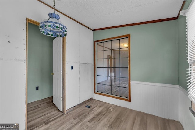 unfurnished dining area featuring a textured ceiling, light wood finished floors, a wainscoted wall, and crown molding