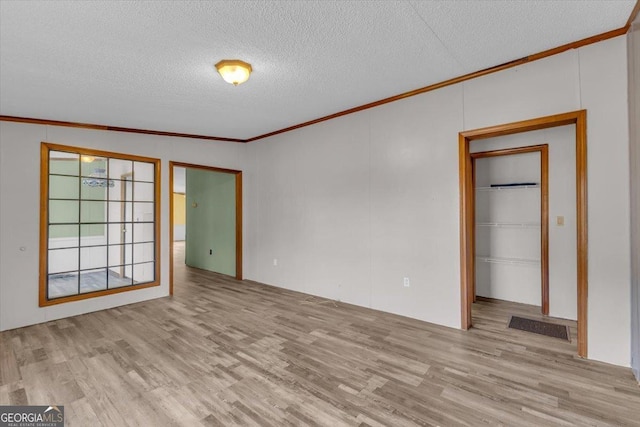 spare room featuring a textured ceiling, ornamental molding, visible vents, and light wood-style flooring