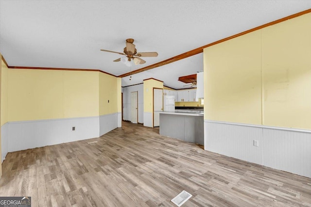 unfurnished living room featuring a wainscoted wall, light wood finished floors, a ceiling fan, and crown molding