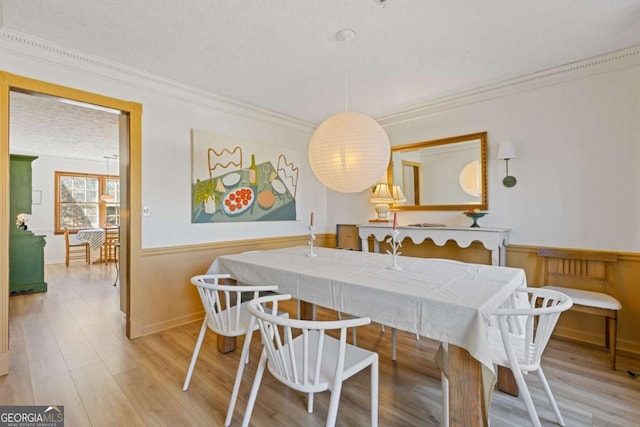 dining area featuring ornamental molding, a wainscoted wall, a textured ceiling, and wood finished floors